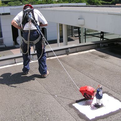 Worker secured with safety harness on rooftop near equipment.