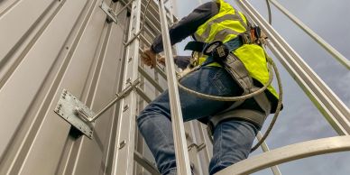 Worker in safety gear climbing a metal ladder on a structure.