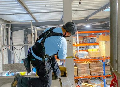 Worker wearing safety harness inspects warehouse shelving.