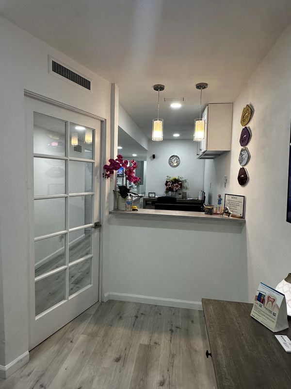 Modern dental office reception with glass door and flowers.