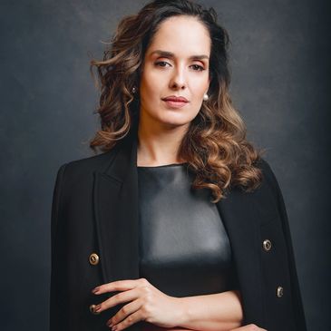 Confident woman with curly hair in a black leather top and blazer.