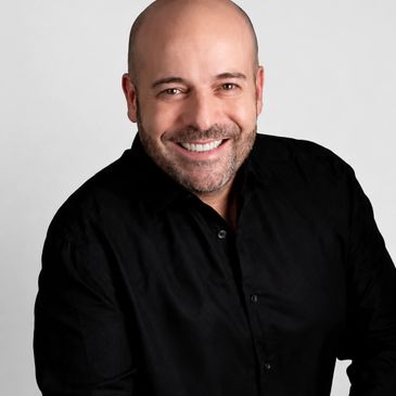 Smiling bald man in a black shirt against a plain background.