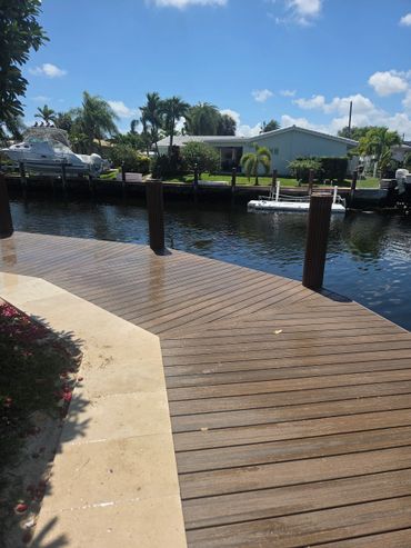 Wooden dock alongside a canal with houses and boats in the background.