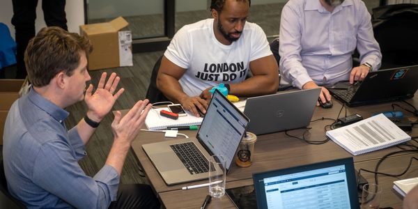 Three men collaborating with laptops and documents in an office meeting.