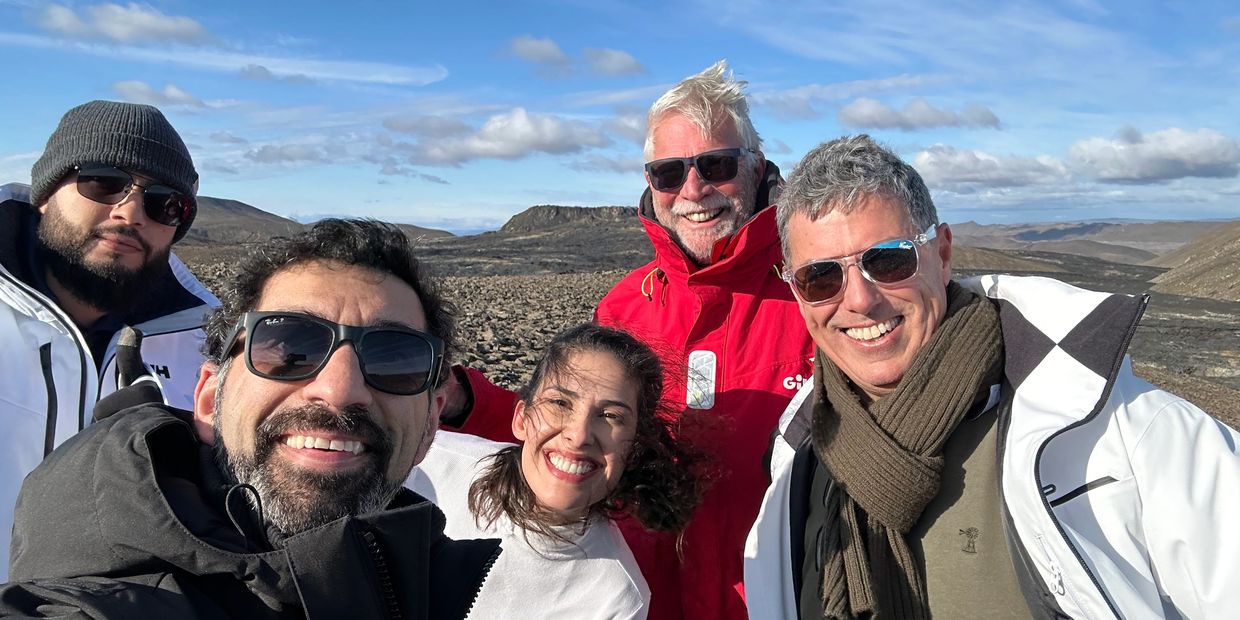 Group of friends smiling outdoors in sunny, rocky terrain with clear skies.