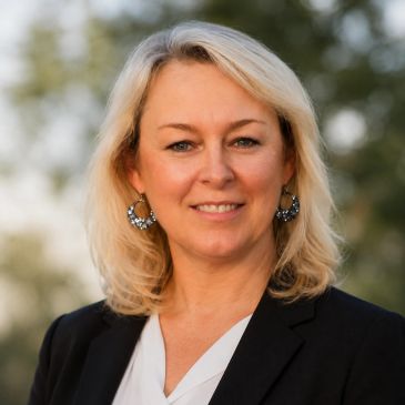 Professional woman smiling outdoors in business attire.