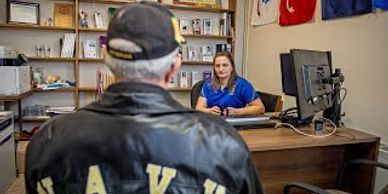 Man in leather jacket talking to a woman at a desk.