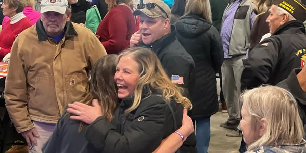 People hugging and socializing in a crowded indoor space.