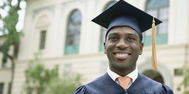 Smiling graduate in cap and gown outdoors.