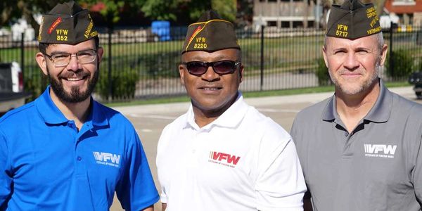 Three men in VFW attire smiling outdoors.