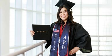 Graduate holding diploma, wearing cap and gown with veteran sash.