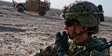 Soldier using radio communication in desert with military vehicle.