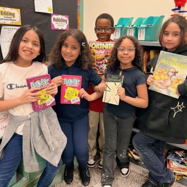 Five children proudly holding various books in a classroom setting.