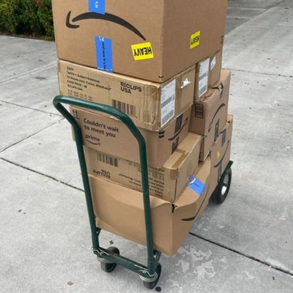 Stack of Amazon boxes on a green hand truck, some marked heavy and with Prime messages.
