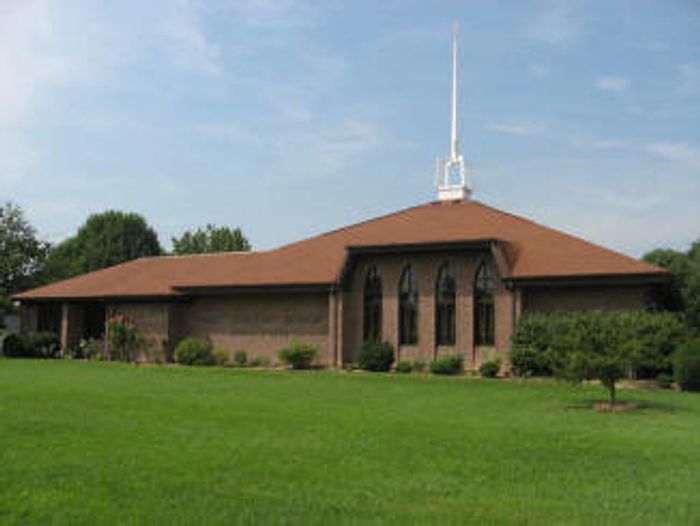 A church with a tall white steeple and brown roof surrounded by green grass.