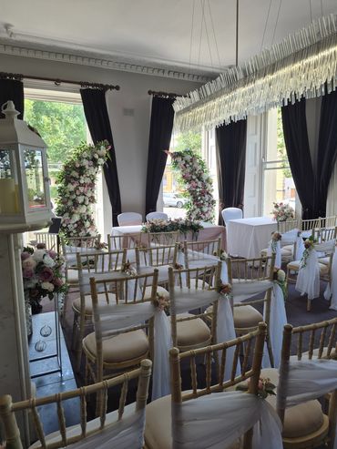 Elegant indoor wedding ceremony setup with floral decorations and draped chairs.