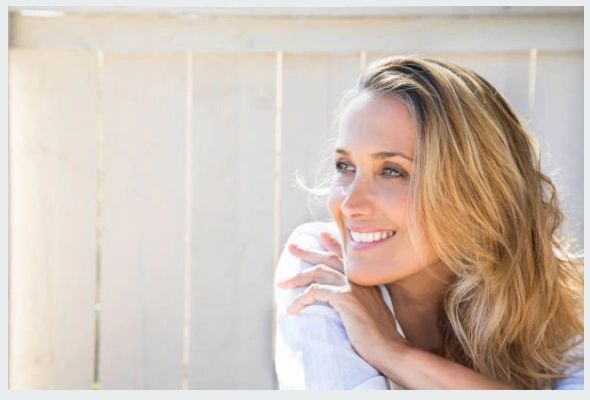 Smiling woman with blonde hair looking to the side outdoors.