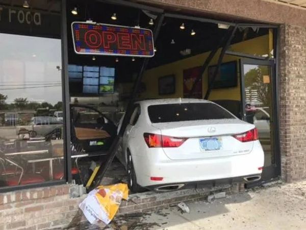 A white car crashed through a restaurant's glass entrance under an 'OPEN' sign.