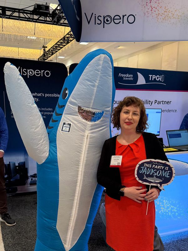 I stand next to a shark mascot at a booth, holding a sign that reads, “This party is JAWSOME.”
