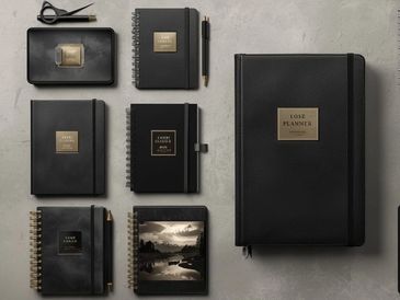 Black leather planners and notebooks arranged on a gray surface.