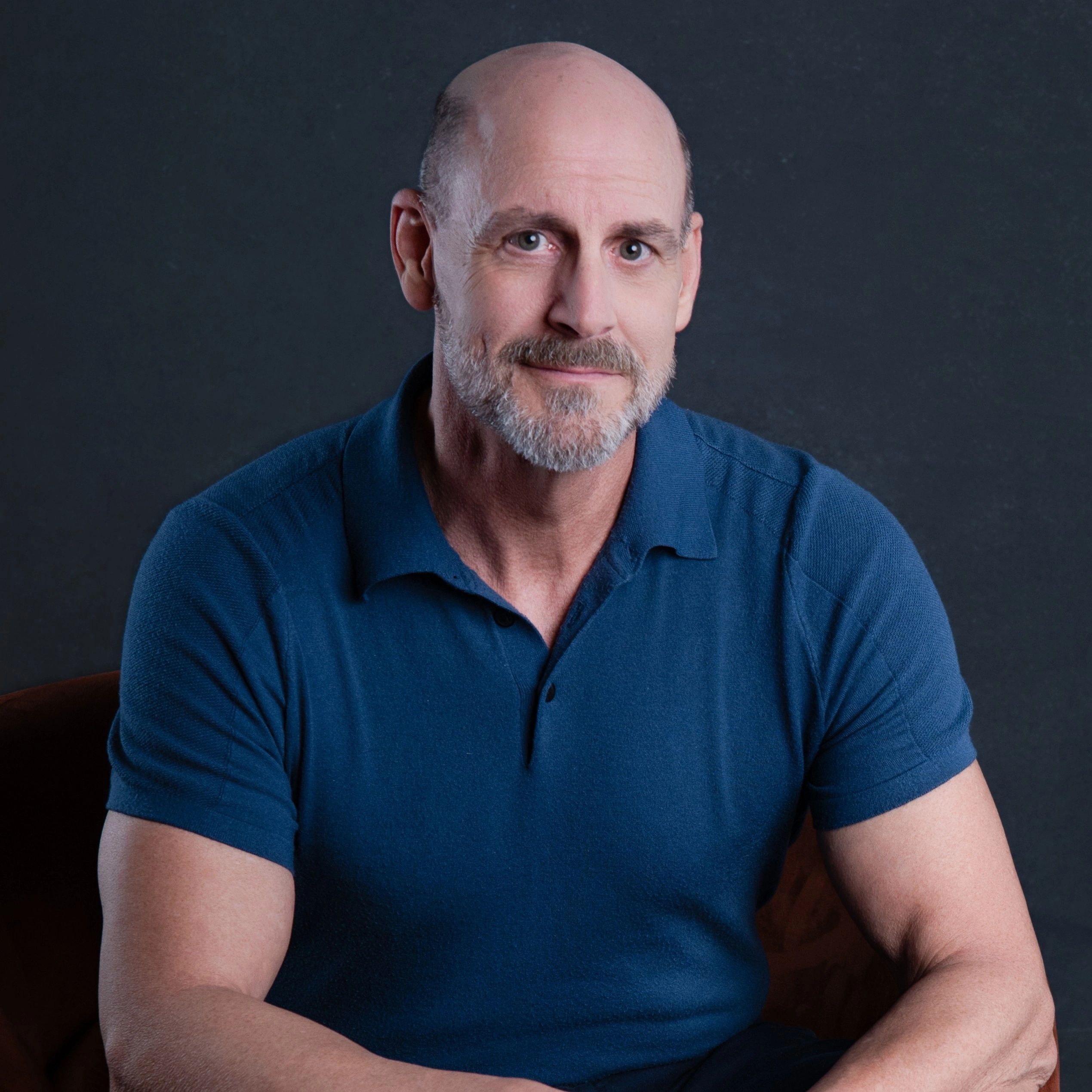 Middle-aged man with a beard wearing a blue polo shirt smiling gently.