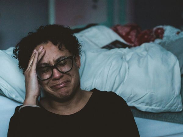 A person with glasses crying and holding their forehead in distress.