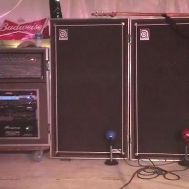 Two large speaker cabinets and audio equipment setup on a concrete floor under a tent.