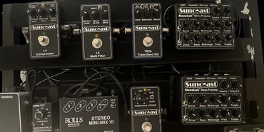 A collection of Suncoast guitar effect pedals and audio equipment on a black board.