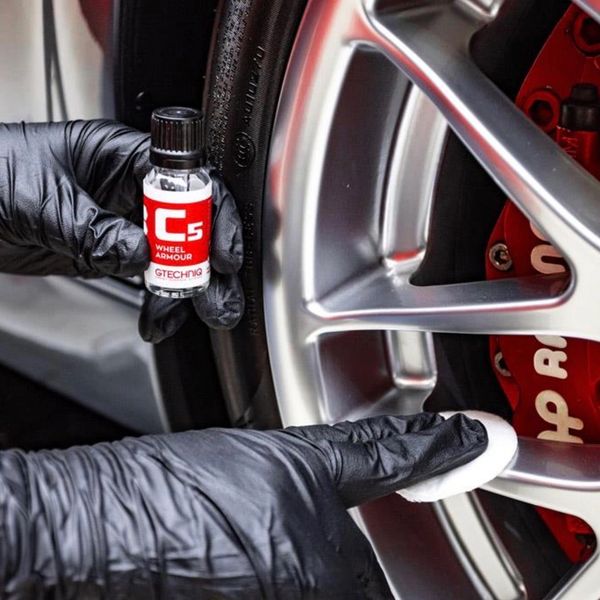 Applying Gtechniq C5 Wheel Armour on a car's alloy wheel with gloves.