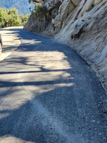 Mountain road winding alongside rocky cliffs under sunlight.