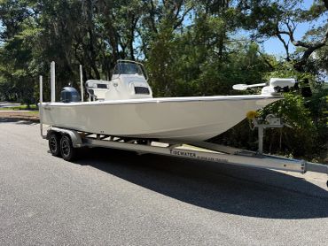 White fishing boat on a trailer parked on a street with trees.