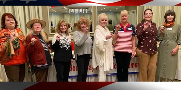 Group of eight women standing in a line, each holding a small object and smiling.