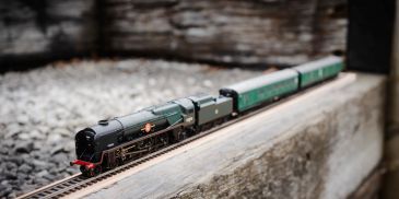 Detailed model steam train on miniature tracks outdoors.