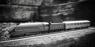 Black and white photo of a vintage model train on wooden tracks.