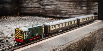 A detailed model train on outdoor tracks with vintage passenger cars.