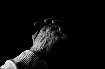 Black background with an older person praying to the Lord Jesus Christ.