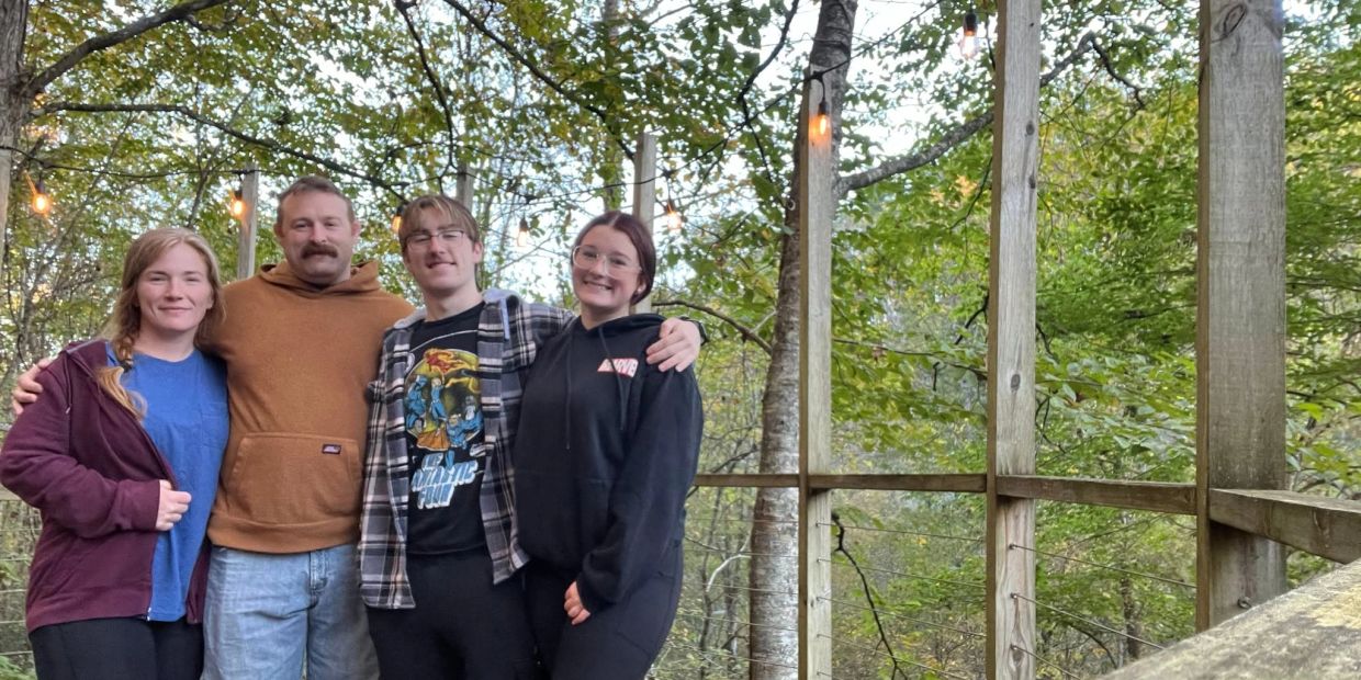 A family smiling on a wooden deck in a forest.