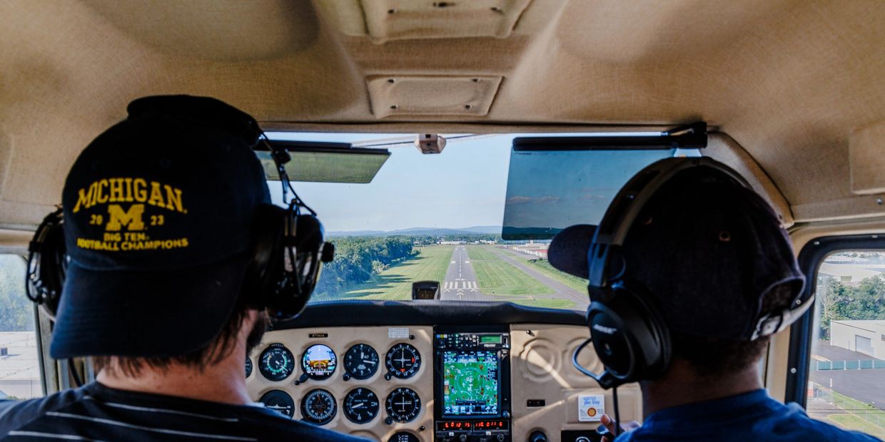 Two pilots approach a runway inside a small aircraft cockpit.