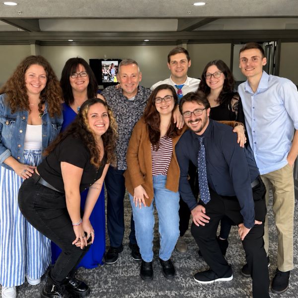 Group photo of nine smiling adults indoors.
