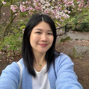 Young woman taking a selfie near blooming pink cherry blossoms in a garden.