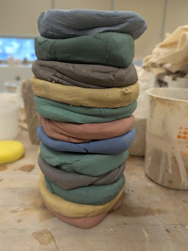 White stoneware clay is colored by using mason stains. The clay is then stacked to create a block.