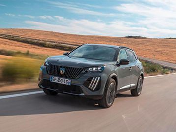 A sleek black SUV driving on a road through a dry, hilly landscape.