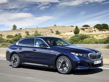 A sleek blue BMW sedan driving on a road with a scenic background.