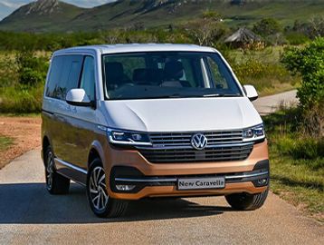 Volkswagen New Caravelle parked on a rural road with mountains in the background.