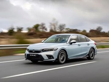 A silver Honda Civic driving on a highway under cloudy skies.