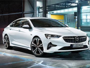 A sleek white Opel sedan parked in a modern urban setting at night.
