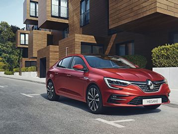 Red Renault Megane parked near modern wooden buildings.