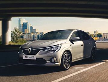 Silver Renault Taliant sedan driving on a city road under a bridge.