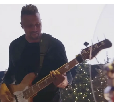 Man playing bass guitar with Christmas tree lights in background.