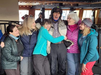 A joyful group of friends in winter gear sharing a hug indoors.